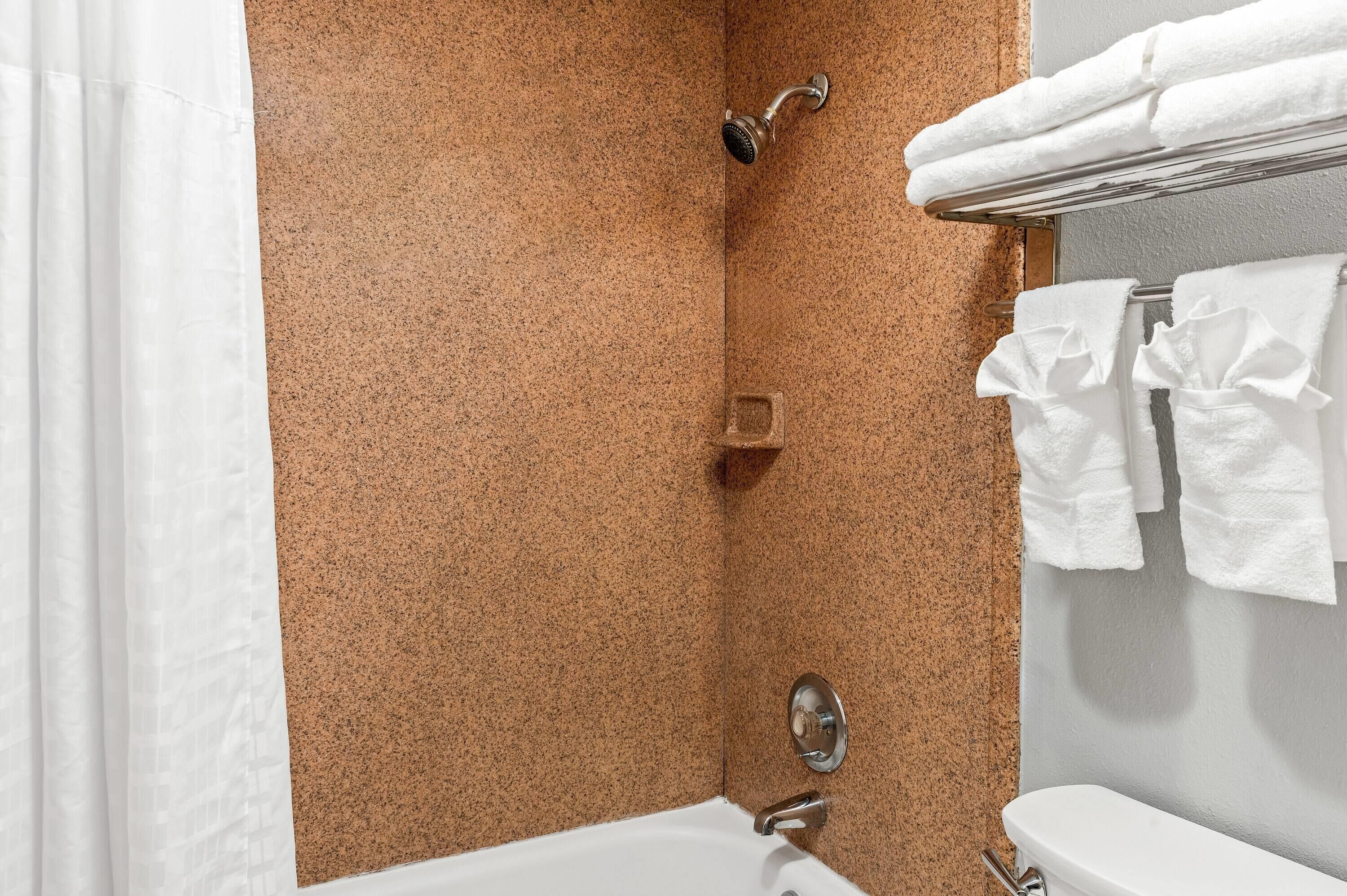 Een badkamer met een bad, douche en toilet. Handdoeken hangen aan een rek.