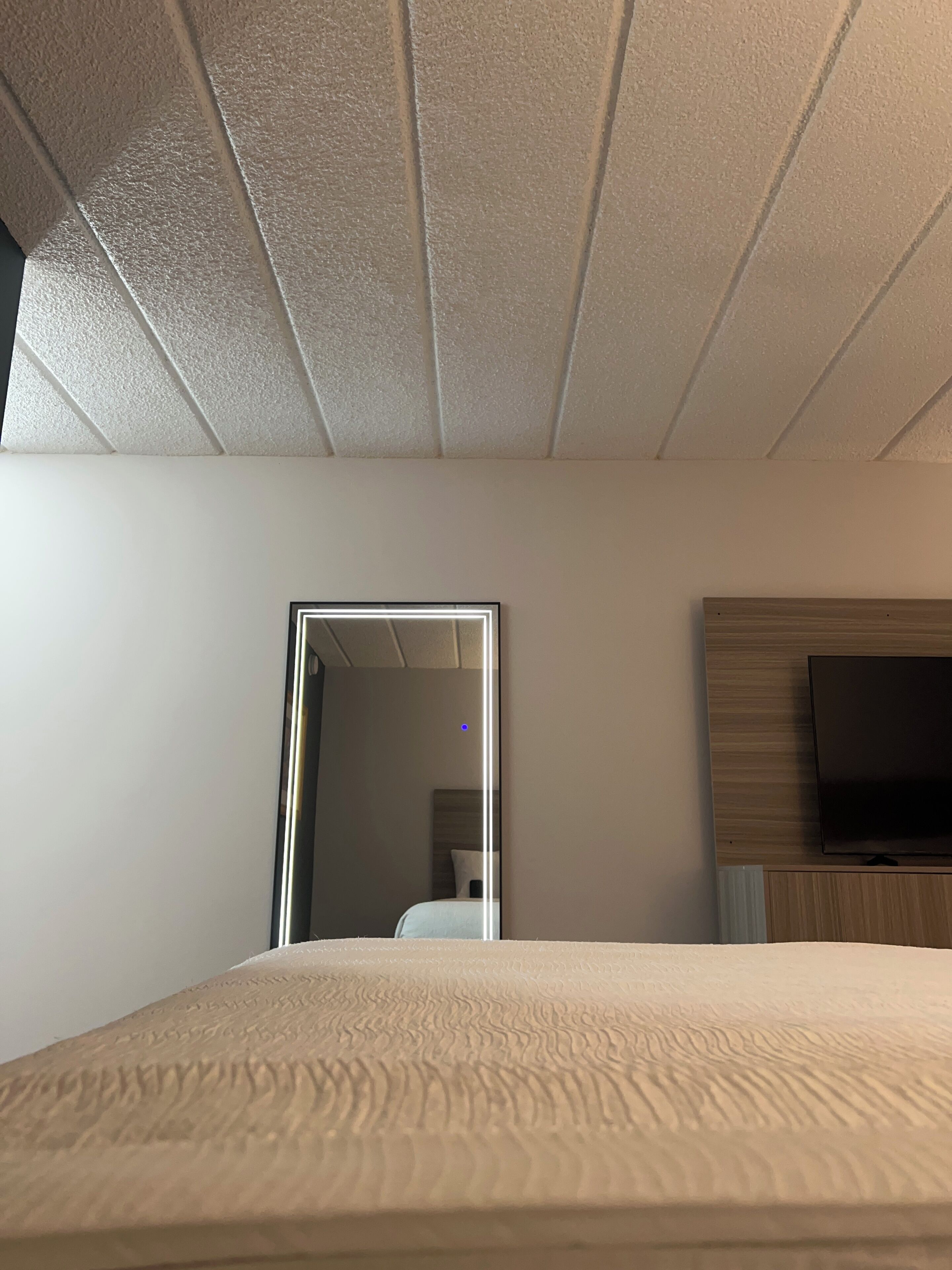 Une chambre à coucher avec un lit, un téléviseur fixé au mur et une porte donnant sur une autre pièce.