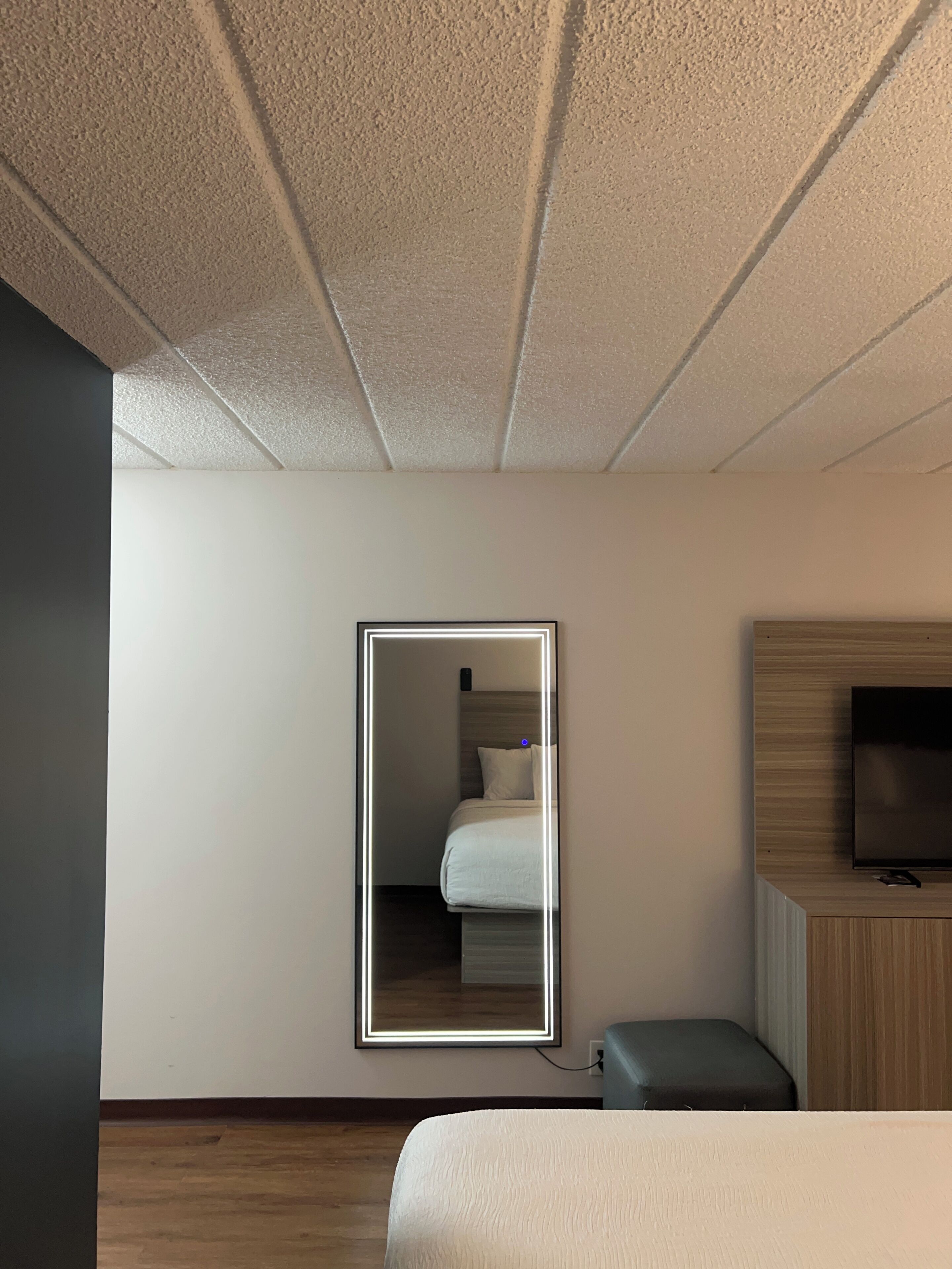 A hotel room with a bed, a TV, a mirror, and a wooden floor.