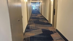 A hotel hallway with carpeted floors, doors on both sides, and overhead lighting. - Baymont by Wyndham Milesburg (Howard)