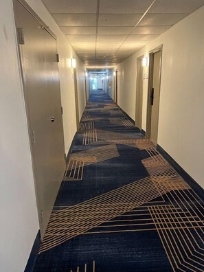 A hotel hallway with carpeted floors, doors on both sides, and overhead lighting. - Baymont by Wyndham Milesburg (Howard)
