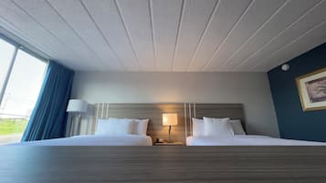 Habitación de hotel con dos camas, una mesita de noche, una lámpara y vistas a zonas verdes.
