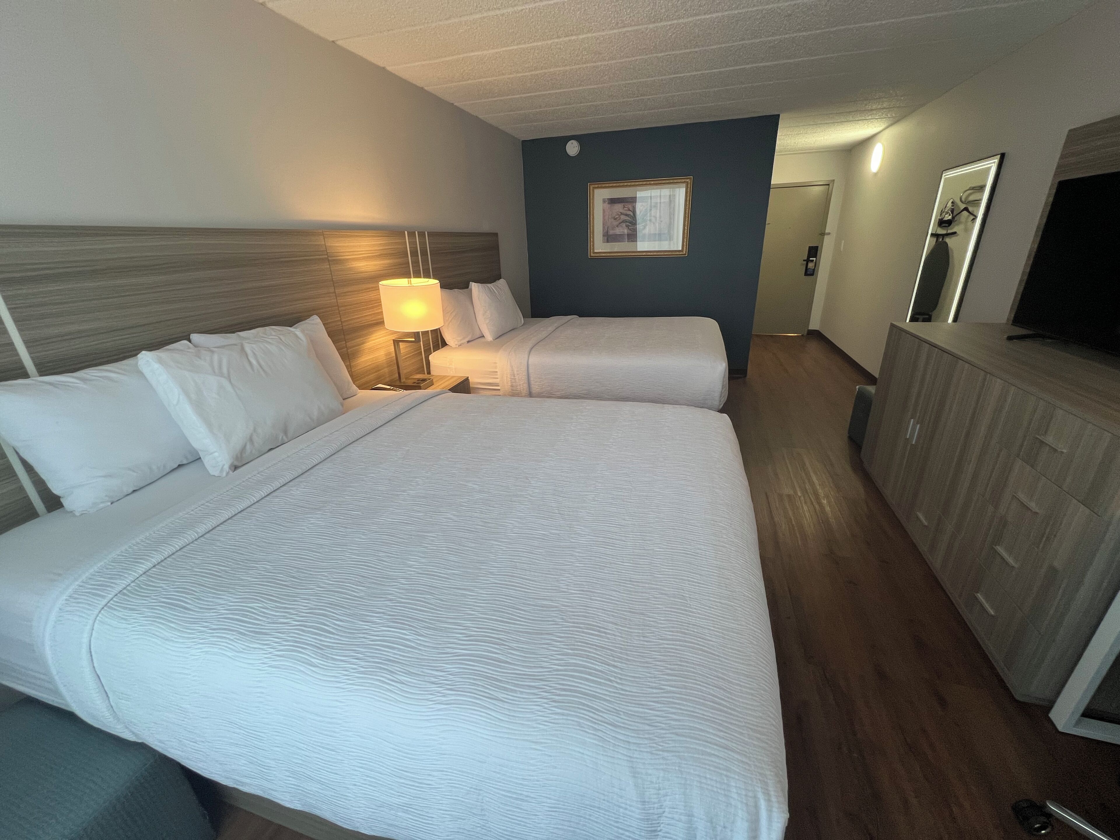 A hotel room with two beds, a nightstand with a lamp, a dresser, and a television.