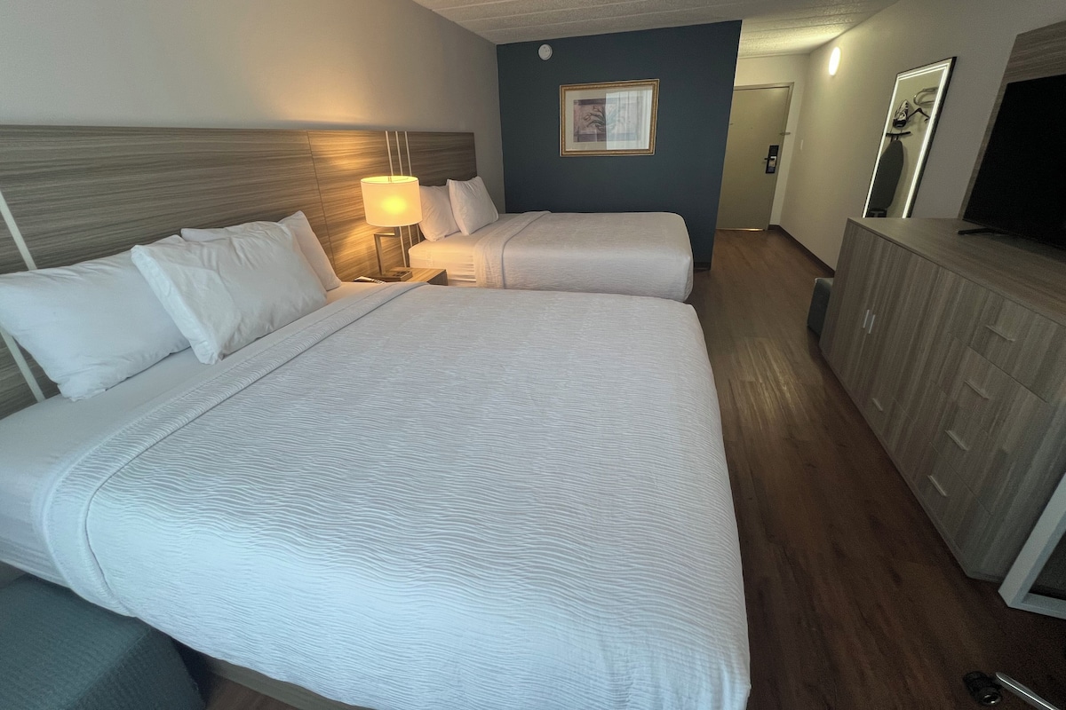 A hotel room with two beds, a nightstand with a lamp, a dresser, and a television.