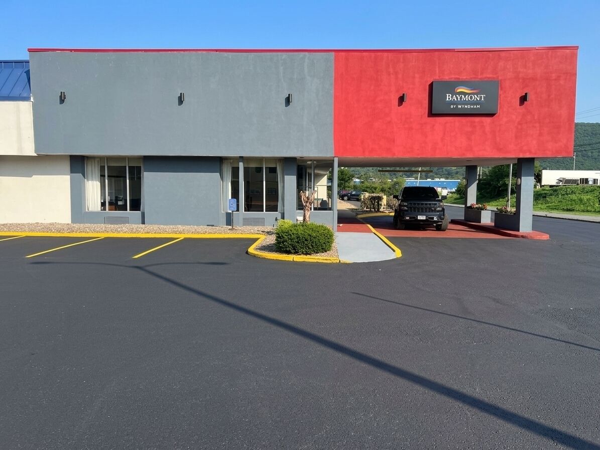 A building with a red and grey facade, a parking lot, and a sign that reads 'Baymont by Wyndham'.