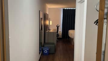 A hotel hallway with a wooden floor, a bed, a desk, and a mirror.
