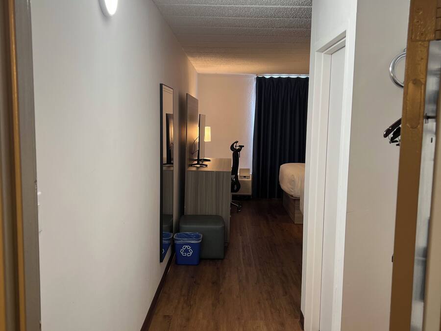 A hotel hallway with a wooden floor, a bed, a desk, and a mirror.