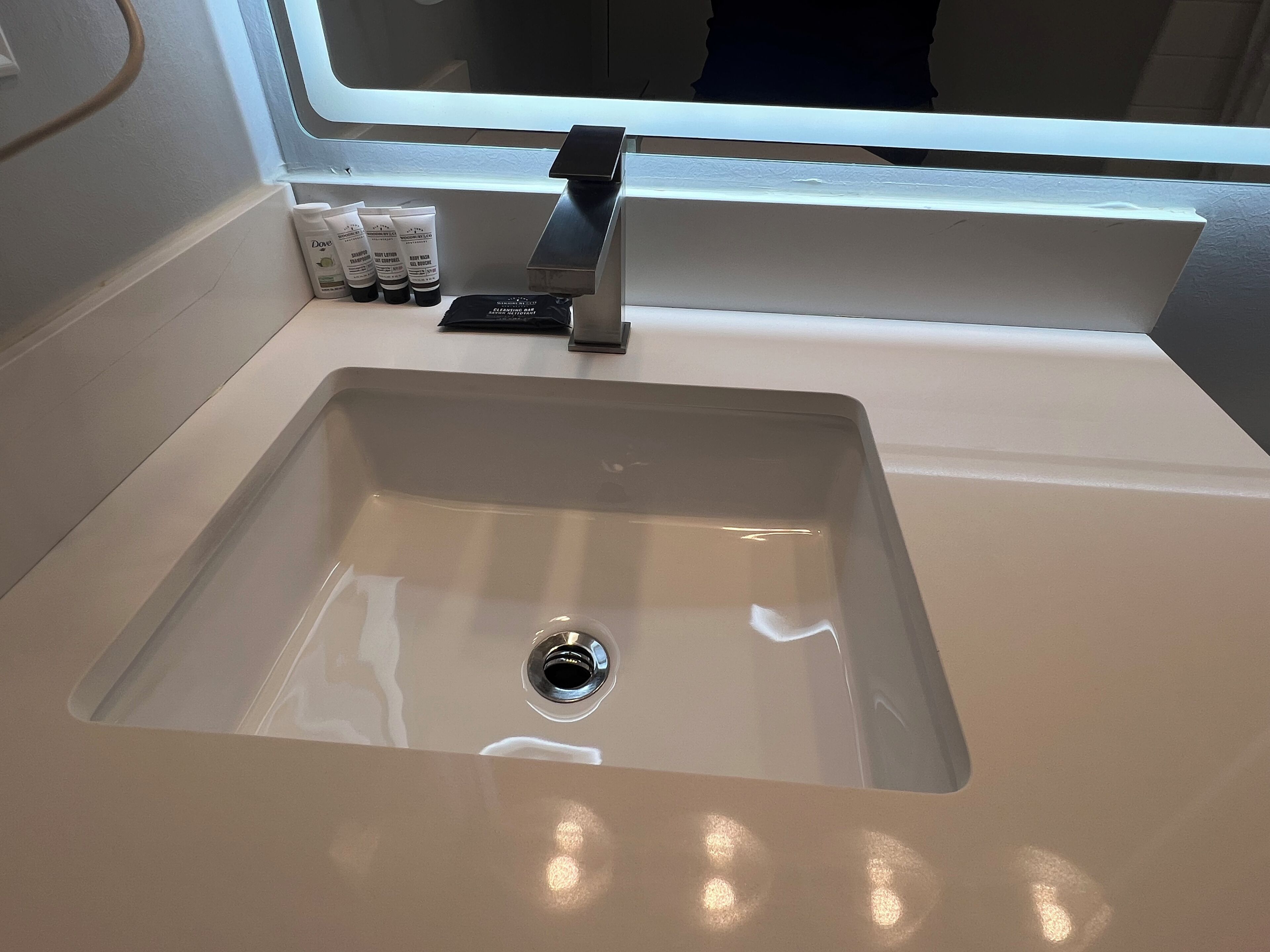 Een wastafel met een moderne kraan, een raam erboven en toiletartikelen op het aanrecht.