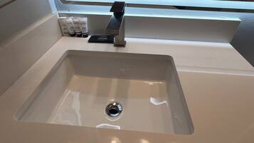 Een wastafel met een moderne kraan, een raam erboven en toiletartikelen op het aanrecht.