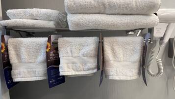Un baño de hotel con toallas blancas en un estante, un secador de pelo y un cartel que promueve la conservación del medio ambiente.