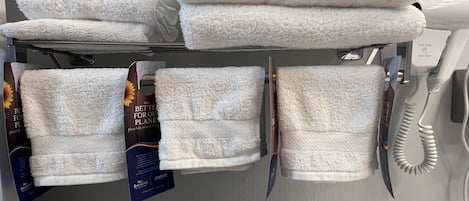 Un baño de hotel con toallas blancas en un estante, un secador de pelo y un cartel que promueve la conservación del medio ambiente.