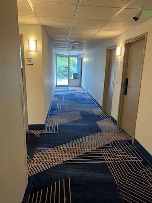 A hotel corridor with a patterned carpet, doors, and wall-mounted lights.