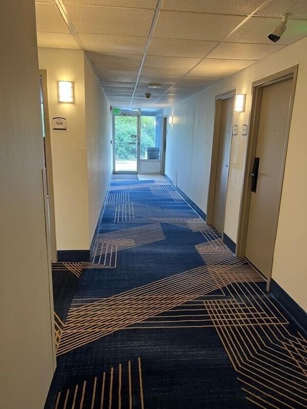 A hotel corridor with a patterned carpet, doors, and wall-mounted lights.