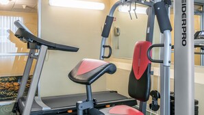 A gym with a treadmill, a red and black weight bench, and a wall-mounted exercise machine. - Baymont by Wyndham Milesburg (Howard)