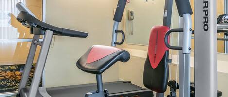 A gym with a treadmill, a red and black weight bench, and a wall-mounted exercise machine.