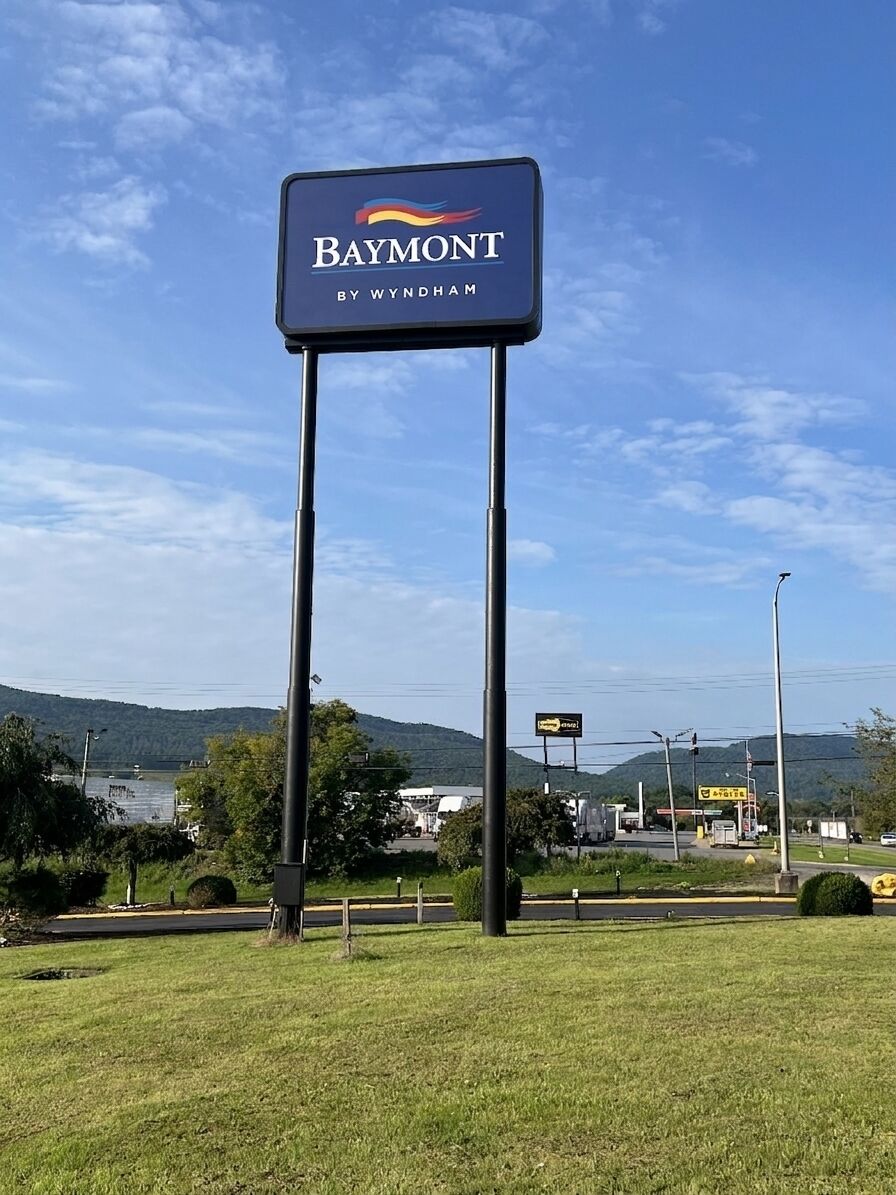 A sign for Baymont by Wyndham with a view of a lake and hills in the background.