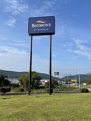 Une enseigne de l’hôtel Baymont by Wyndham, avec en arrière-plan un lac et des collines.