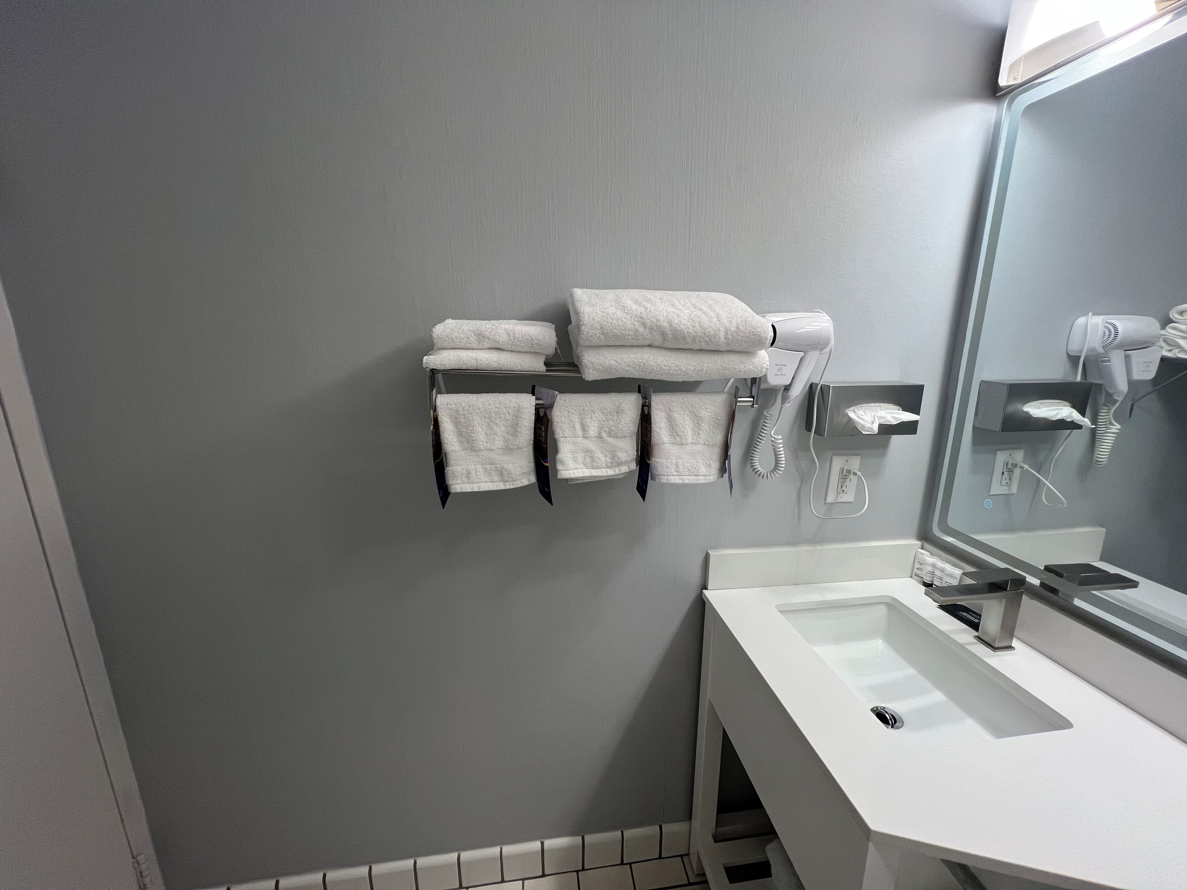 A bathroom with a white sink, a mirror, and a towel rack with folded towels.