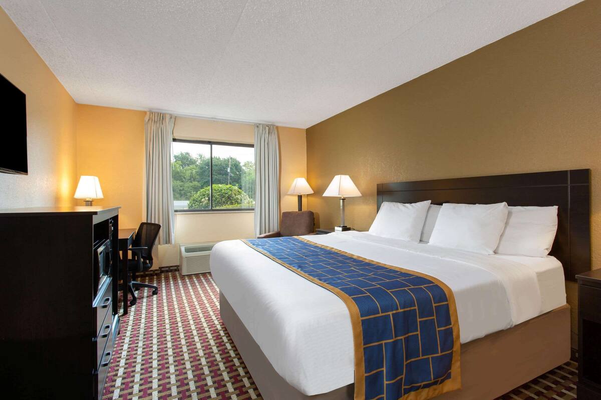 Une chambre d’hôtel avec un grand lit, deux lampes de chevet, un bureau avec une chaise et une fenêtre avec des rideaux.