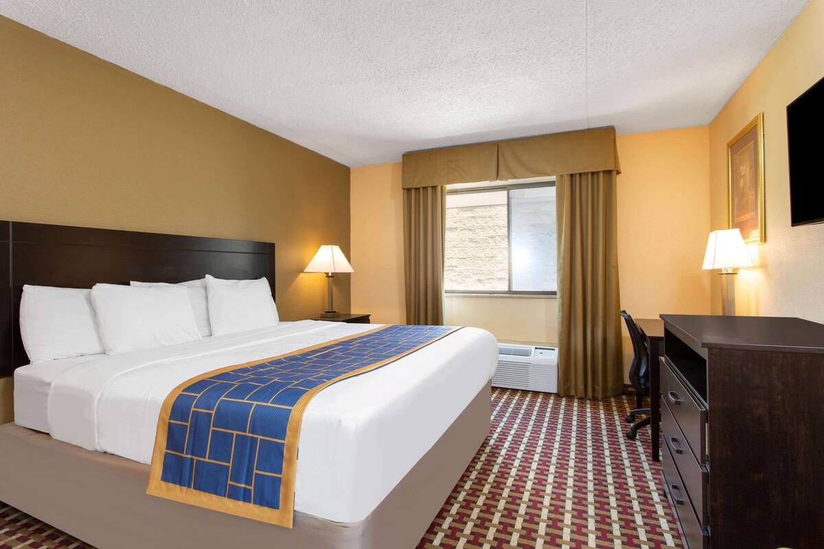Une chambre d’hôtel avec un grand lit, deux tables de chevet avec des lampes, un bureau, une chaise et un téléviseur fixé au mur.
