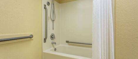A bathroom with a bathtub, grab bars, and a shower head.