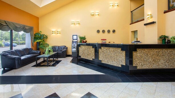 A reception area with a black leather sofa, a reception desk, and a plant. - Days Inn by Wyndham Hillsborough (Hillsborough)