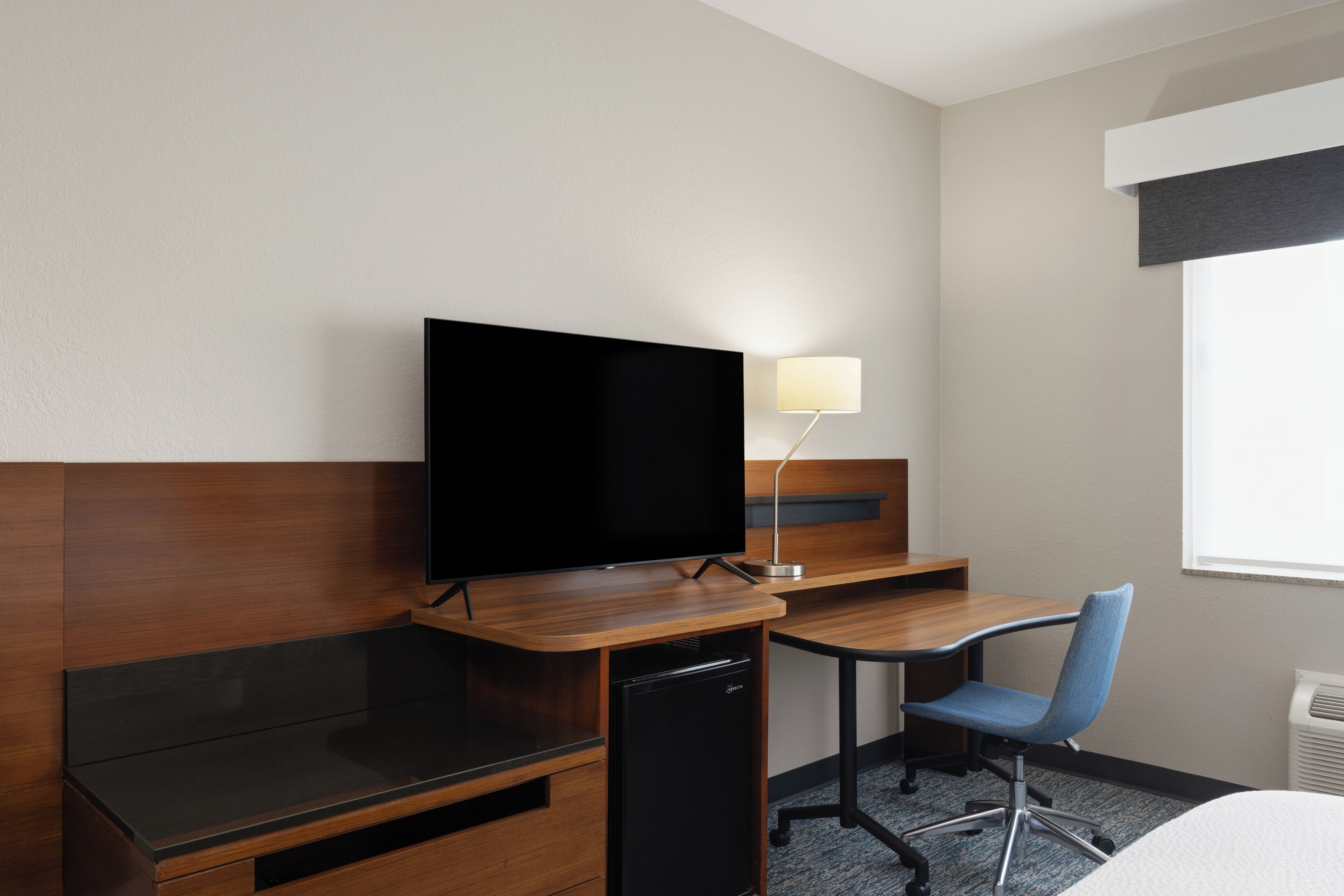 Habitación de hotel con escritorio de madera, televisión, una silla, lámpara y cama.