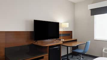 Habitación de hotel con escritorio de madera, televisión, una silla, lámpara y cama.