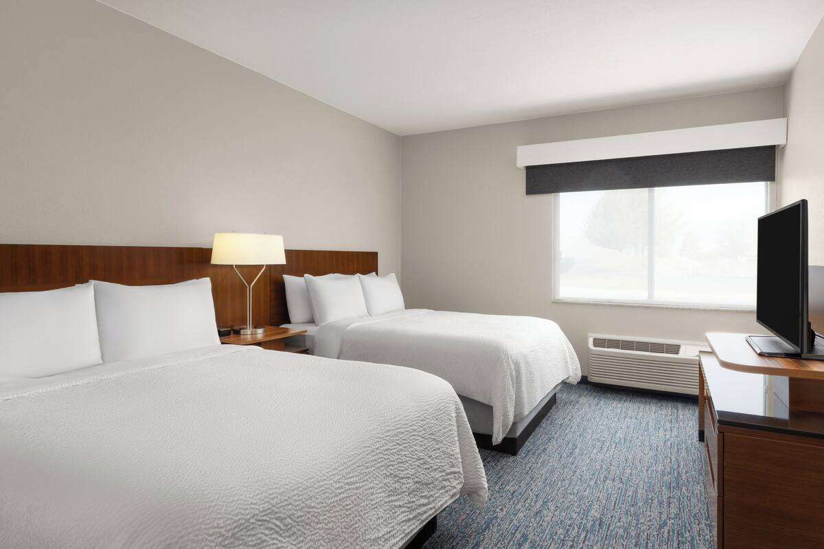 A hotel room with two beds, a desk with a TV, a lamp, and a window with a view.