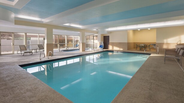 An indoor swimming pool with clear water, surrounded by lounge chairs and a view of the outside.