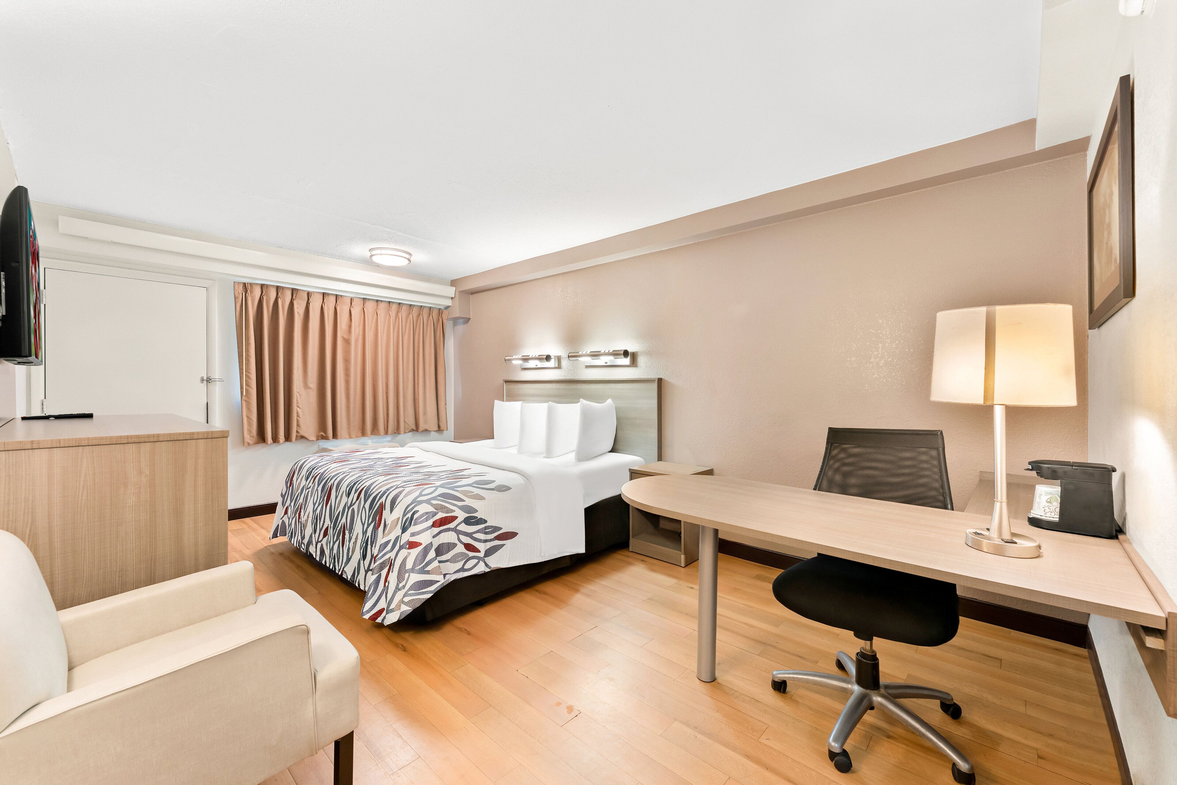 Una habitación de hotel con una cama, un escritorio, una silla, un televisor y una ventana con cortinas.