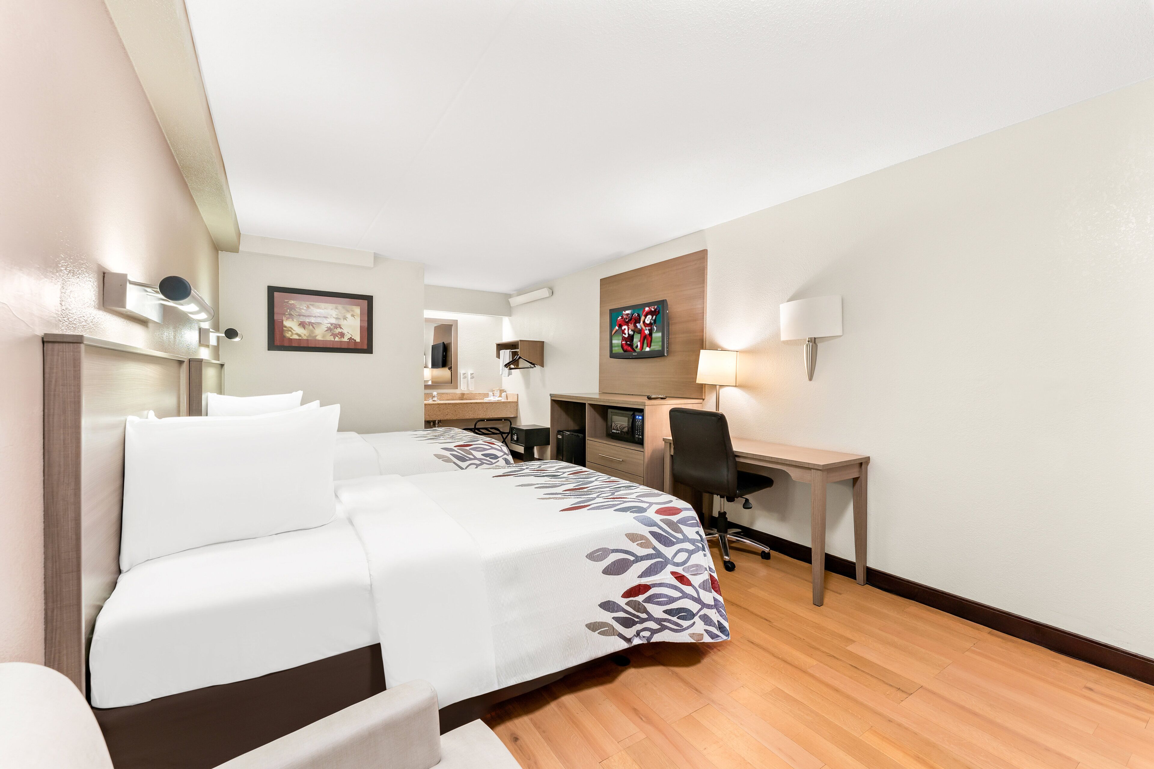 A hotel room with a bed, desk, chair, and a small table.
