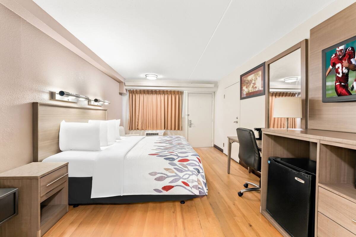 Een hotelkamer met een bed, een bureau, een stoel, een koelkast en een raam met gordijnen.