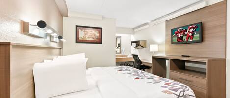 A hotel room with a bed, a desk, a chair, a TV, and a framed picture on the wall.