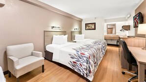 Een hotelkamer met een groot bed, een bureau, een stoel en een kleine kitchenette.
