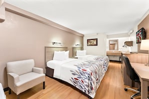 Ein Hotelzimmer mit einem großen Bett, einem Schreibtisch, einem Stuhl und einer kleinen Küchenzeile.