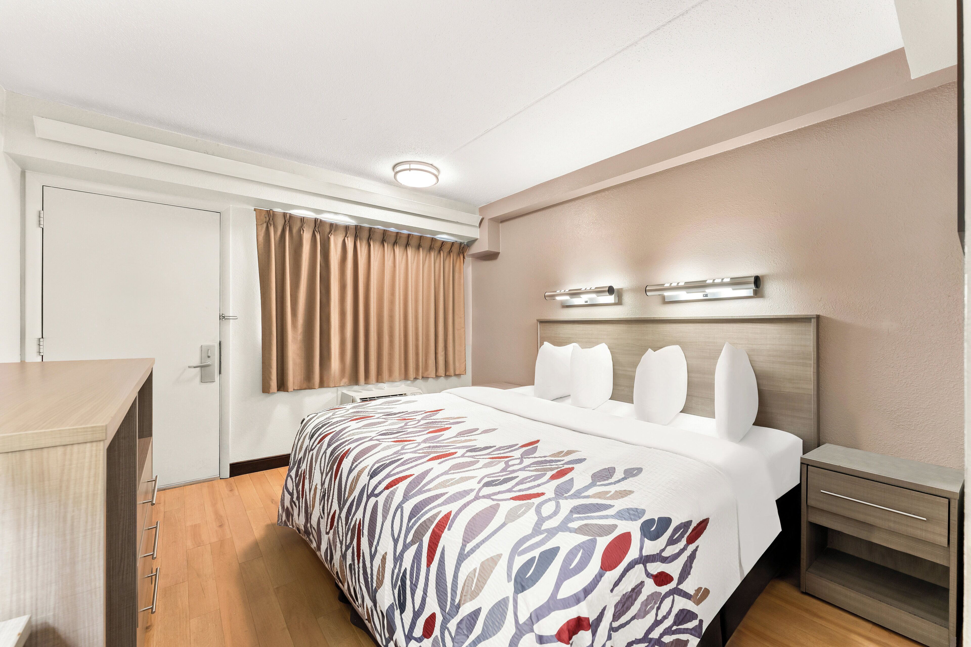 Habitación de hotel con cama, mesitas de noche, escritorio, ventana con cortinas e iluminación en el techo.