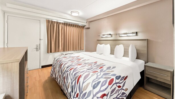 Une chambre d’hôtel comprenant un lit, des tables de chevet, un bureau, une fenêtre avec des rideaux et un luminaire au plafond.