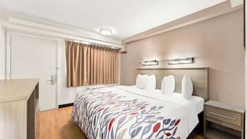 Habitación de hotel con cama, mesitas de noche, escritorio, ventana con cortinas e iluminación en el techo.