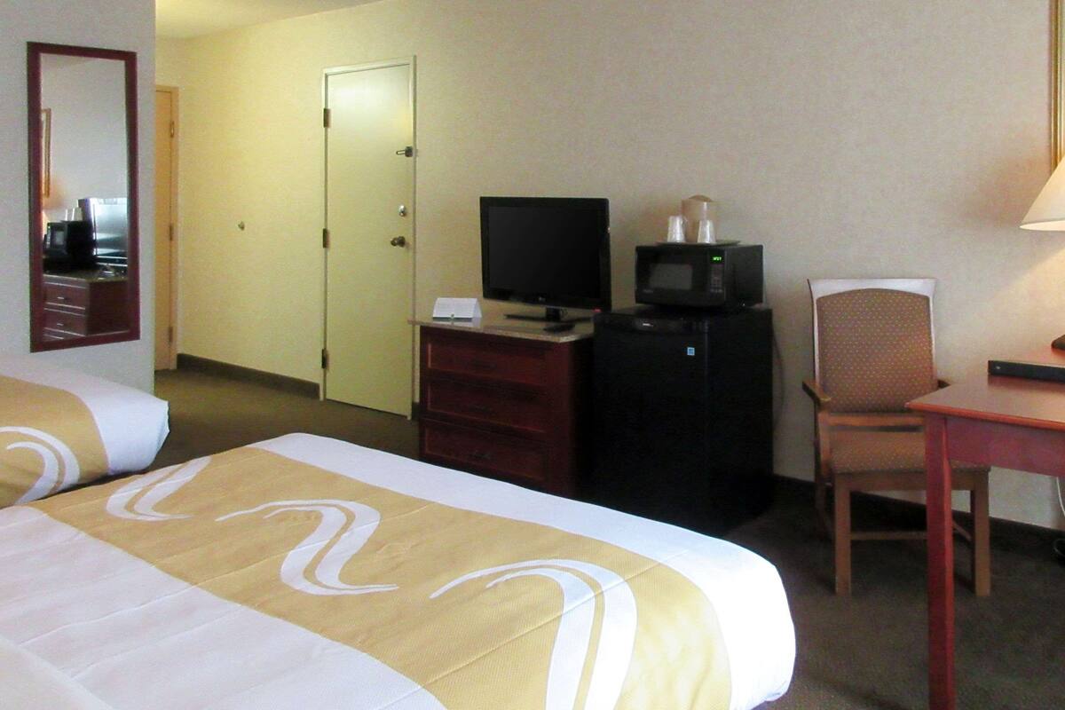 A hotel room with two beds, a television, a microwave, a desk, and a chair.