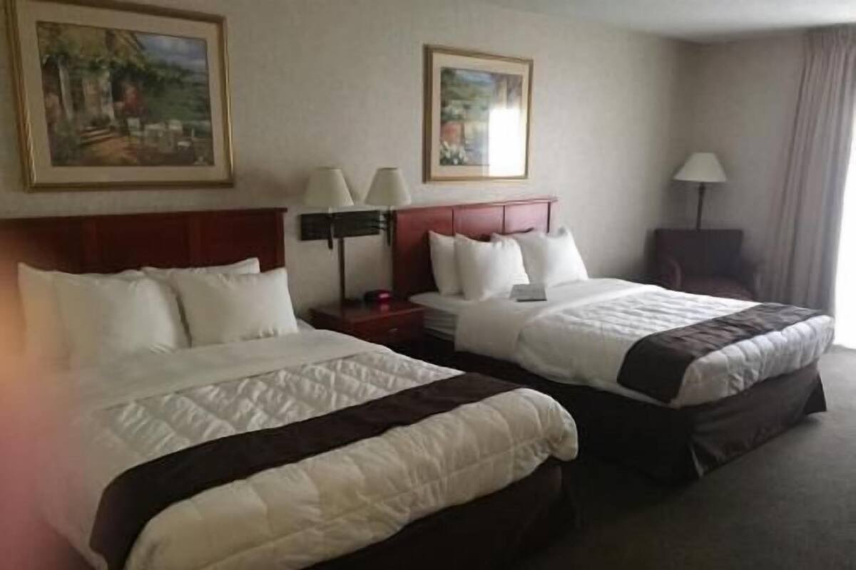 A hotel room with two beds, a nightstand, a lamp, and two framed pictures on the wall.