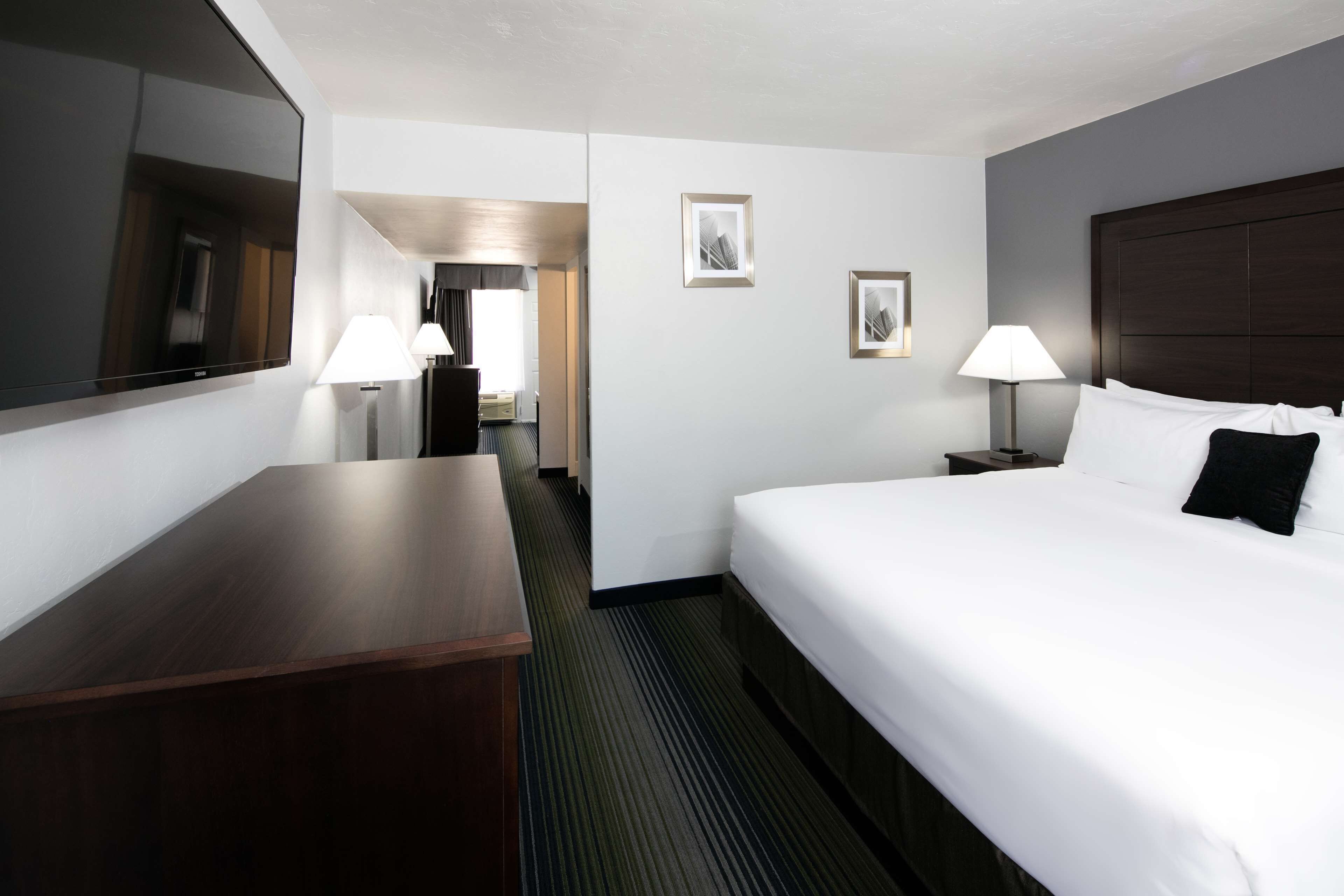 Una habitación de hotel con una cama grande, un escritorio, un televisor de pantalla plana, dos lámparas de noche y cuadros en la pared.