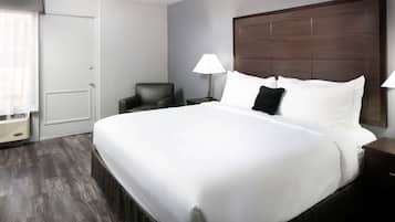 Ein Hotelzimmer mit einem großen Bett, einem Sessel, einem Nachttisch, einer Lampe und einem Fenster mit Jalousien.