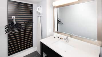 Un baño moderno con un espejo grande, un lavamanos blanco y un perchero negro.