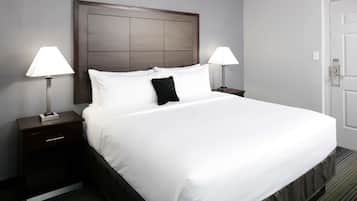 A hotel room with a large bed, two bedside tables with lamps, a wooden headboard, and a door.