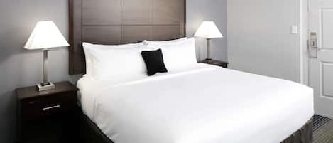 A hotel room with a large bed, two bedside tables with lamps, a wooden headboard, and a door.