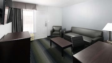 Une chambre d’hôtel avec un bureau en bois foncé, un canapé en cuir, un fauteuil assorti, une petite table basse et une lampe sur une table d’appoint.