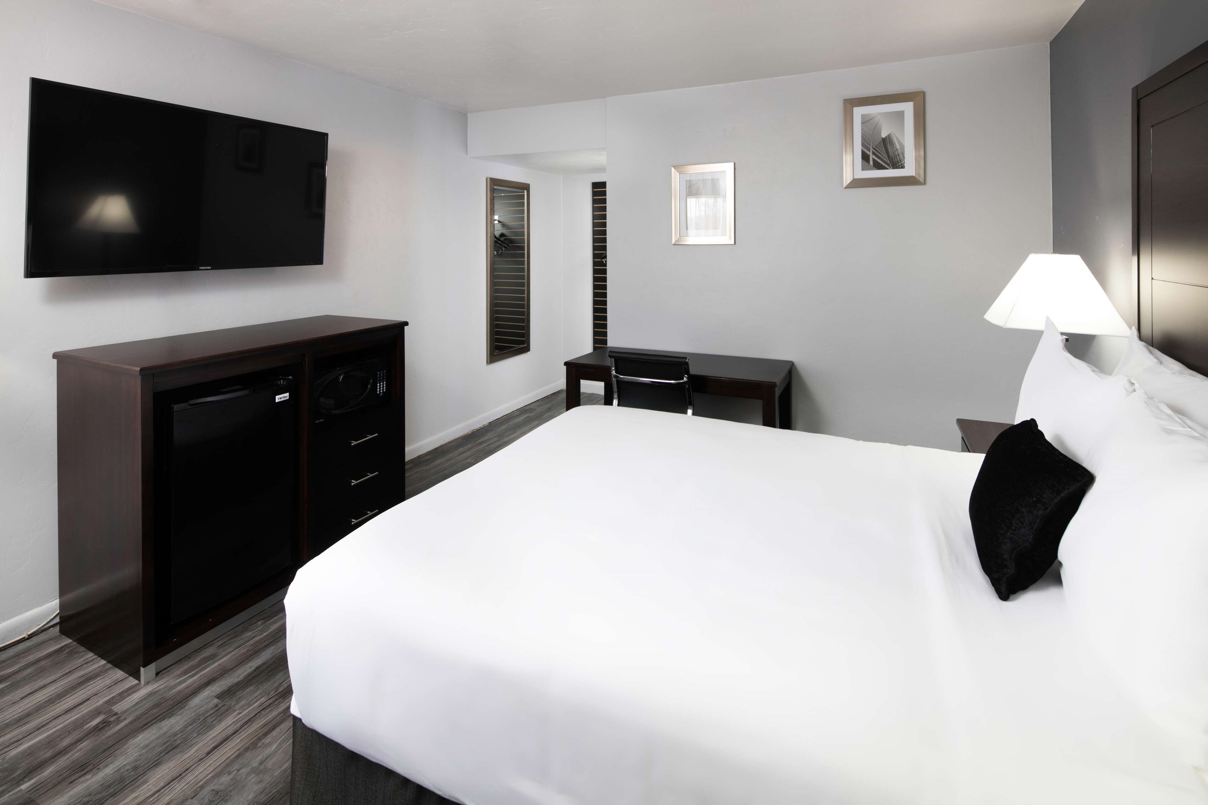 Una habitación de hotel con una cama grande, un televisor en la pared, un escritorio con una silla y una lámpara.
