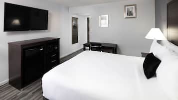 Una habitación de hotel con una cama grande, un televisor en la pared, un escritorio con una silla y una lámpara.