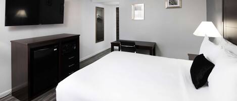 Una habitación de hotel con una cama grande, un televisor en la pared, un escritorio con una silla y una lámpara.